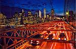 illuminated Brooklyn Bridge with fast cars in the evening with the famous Manhattan skyline in the back, New York City