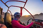 Young woman with head wrapped in scarf driving beach buggy in desert, Hurghada, Al Bahr al Ahmar, Egypt