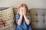 Girl on sofa covering her face with hands