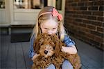 Portrait of girl kissing red haired puppy on front porch