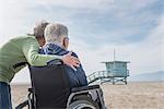 Senior man in wheelchair with wife looking out from beach, Santa Monica, California, USA