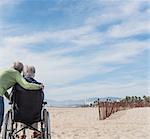 Rear view of senior man in wheelchair with wife looking out from beach, Santa Monica, California, USA