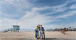 Senior man in wheelchair with wife pointing from beach, Santa Monica, California, USA