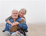 Portrait of senior man in wheelchair with wife and dog at beach, Santa Monica, California, USA