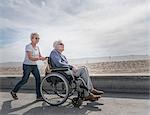 Senior woman pushing husband in wheelchair at beach, Santa Monica, California, USA