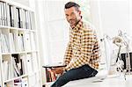 Portrait of male designer sitting on desk in creative studio