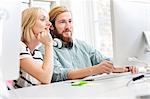 Male and female designers looking at desktop computer in creative studio