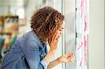 Female digital designer making phone call and looking at adhesive notes on office wall