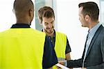 Two men wearing hi vis vests, having discussion with businessman