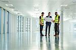 Three men standing in empty office, looking at plans