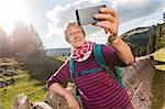 Senior woman, leaning against wall in rural setting, taking selfie, using smartphone, Geneva, Switzerland, Europe