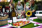 Group of people at garden party, bottle of wine and vegetable kebabs in foreground