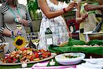 Group of people at garden party, holding wine glasses, making a toast, food on serving plates on table, mid section