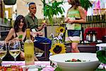 Group of people at garden party, holding wine glasses, bottle of wine and food on serving dishes in foreground