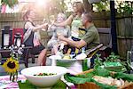 Group of people at garden party, holding wine glasses, making a toast, bottles of wine in ice bucket served food in foreground