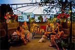 Group of people at garden party, sitting under pergola at dusk, drinking wine