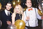 Portrait of three people at party, surrounded by balloons, holding champagne glasses