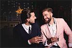 Two men at party, holding drinks, laughing