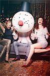 Friends sitting together at party, man holding snowman head in front of face, women laughing