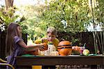 Boy and sister carving pumpkins on garden table