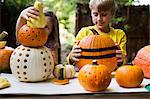 Girl and brother stacking carved pumpkins on garden table