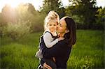 Portrait of woman kissing her daughter in sunlit field