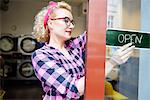 Female small business owner putting up open sign on laundrette door