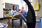 Two women sitting in laundrette reading magazine and looking at smartphone