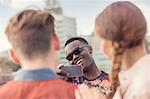 Young man photographing friends at roof party in London, UK