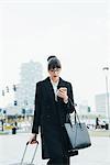 Businesswoman using mobile and pulling trolley luggage, Milan, Italy