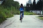 Rear view of teenage girl cycling along rural road