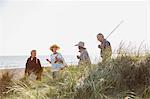 Senior couples with fishing pole walking in sunny beach grass