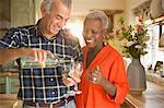 Smiling senior couple pouring white wine in kitchen