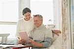 Smiling mature couple using digital tablet at table on sunny sun porch