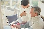 Mature couple drinking coffee and using digital tablet on porch