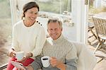 Portrait smiling mature couple using digital tablet and drinking coffee on sun porch