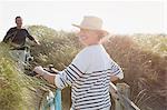 Portrait smiling mature woman walking bicycle on sunny beach grass path