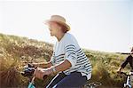 Playful mature woman riding bicycle on sunny beach grass path