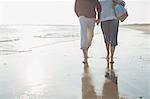 Affectionate barefoot mature couple walking, holding hands in sunny ocean beach surf