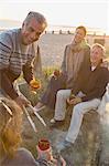 Smiling mature couples drinking wine and barbecuing on sunset beach