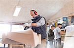 Senior carpenter using sander, sanding wood boat in workshop