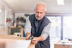 Focused senior male carpenter using jack plane on wood boat in workshop