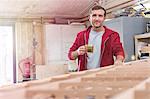 Portrait confident male carpenter drinking tea at wood boat in workshop