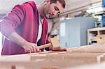 Male carpenter using wood mallet on boat in workshop