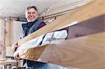 Smiling male carpenter carrying finished wood in workshop