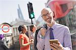 Portrait smiling businessman with cell phone on sunny urban street, London, UK