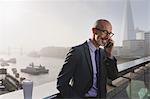 Businessman talking on cell phone on sunny, urban bridge, London, UK