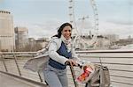 Portrait smiling woman bike riding on bridge over Thames River near Millennium Wheel, London, UK