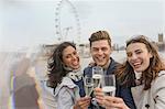 Portrait enthusiastic, smiling friends celebrating, toasting champagne near Millennium Wheel, London, UK