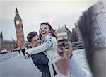 Playful couple tourists being photographed on bridge near Big Ben, London, UK